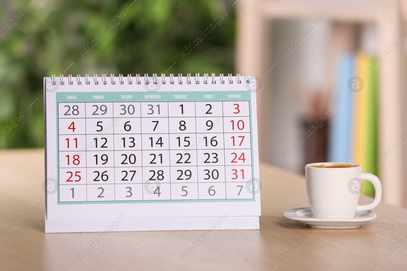 Photo of Calendar and cup of coffee on wooden table against blurred background