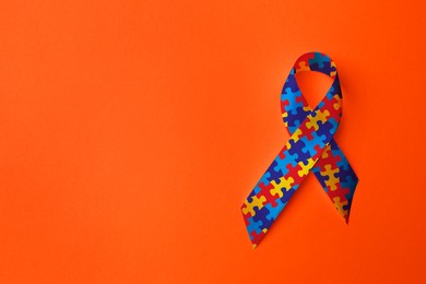 World Autism Awareness Day. Colorful puzzle ribbon on orange background, top view with space for text