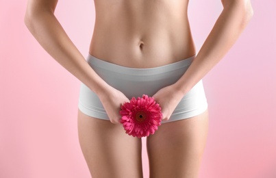 Young woman holding flower near underwear on color background. Gynecology