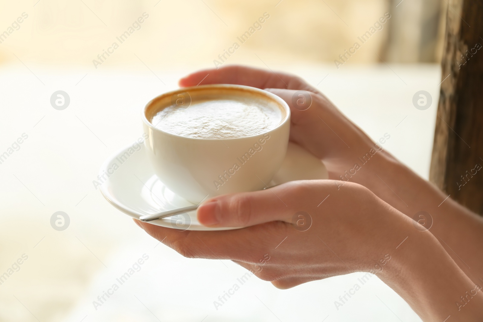 Photo of Young woman with cup of delicious coffee on blurred background