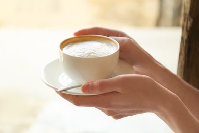 Young woman with cup of delicious coffee on blurred background