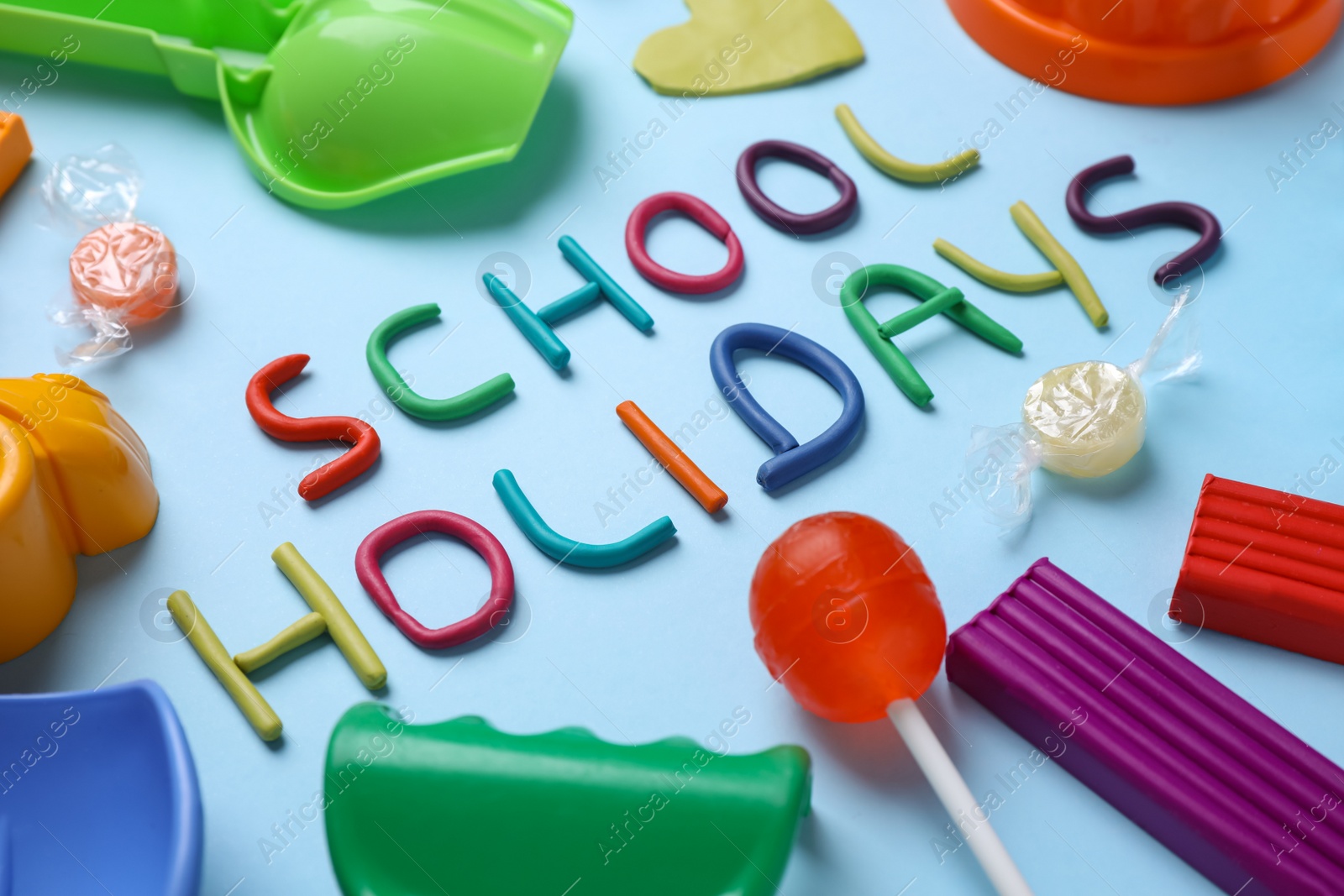 Photo of Composition with phrase School Holidays made of modeling clay on light blue background