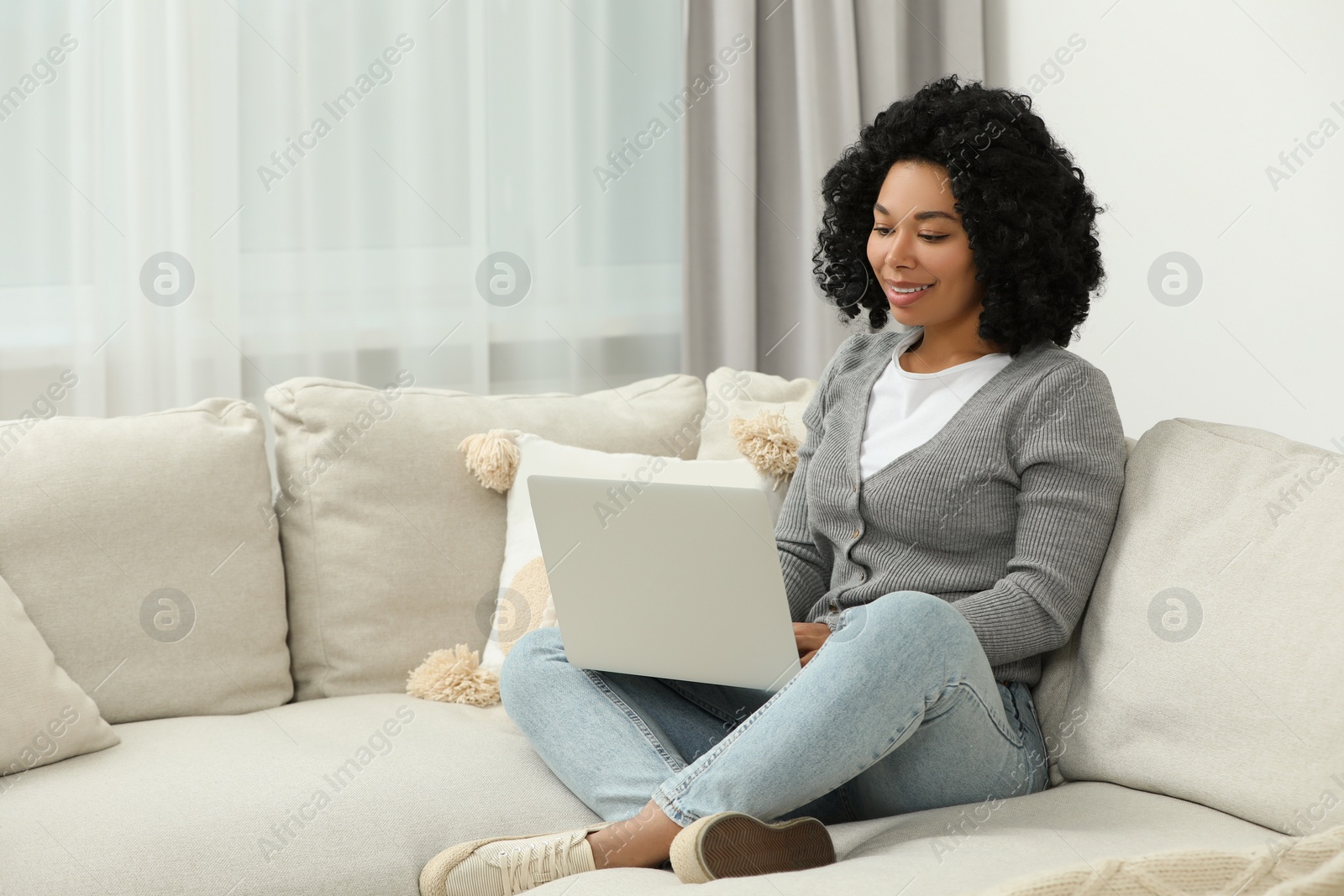Photo of Happy young woman using laptop on sofa indoors. Space for text