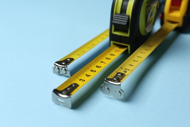 Photo of Tapes measure on light blue background, closeup. Construction tool