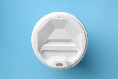One paper cup with white lid on light blue background, top view. Coffee to go