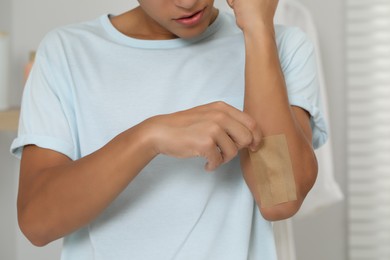 Photo of Man putting sticking plaster onto elbow indoors, closeup