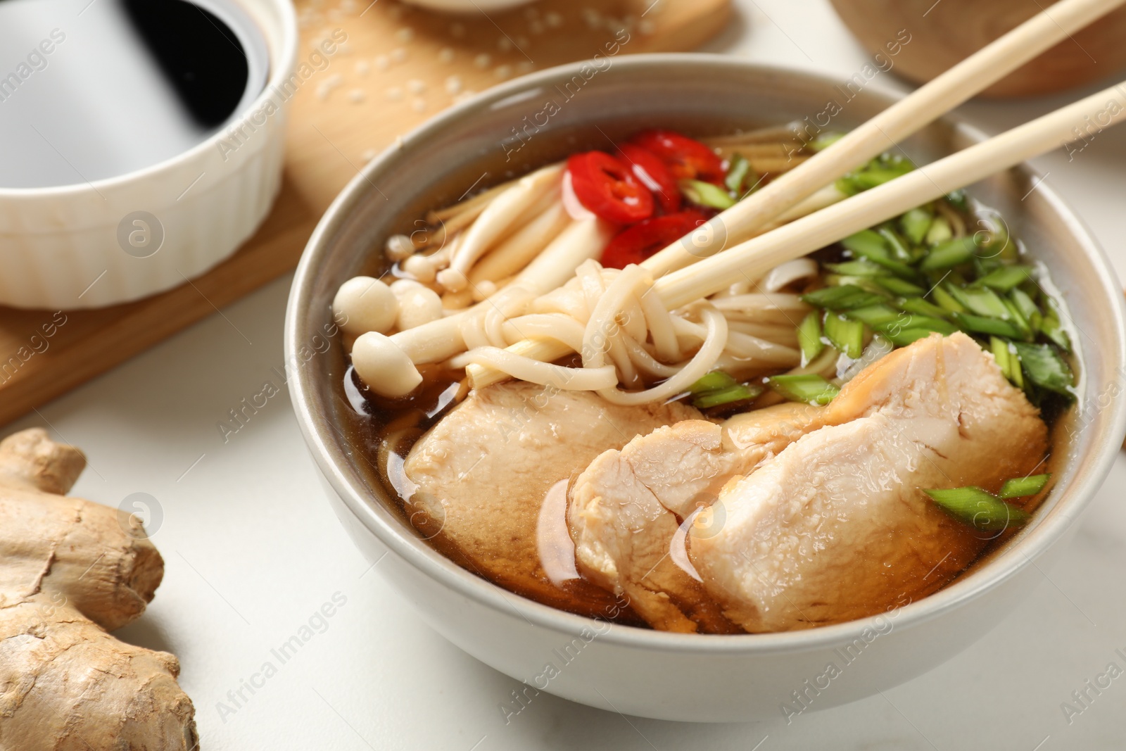 Photo of Delicious ramen with meat and ingredients on white marble table, closeup. Noodle soup