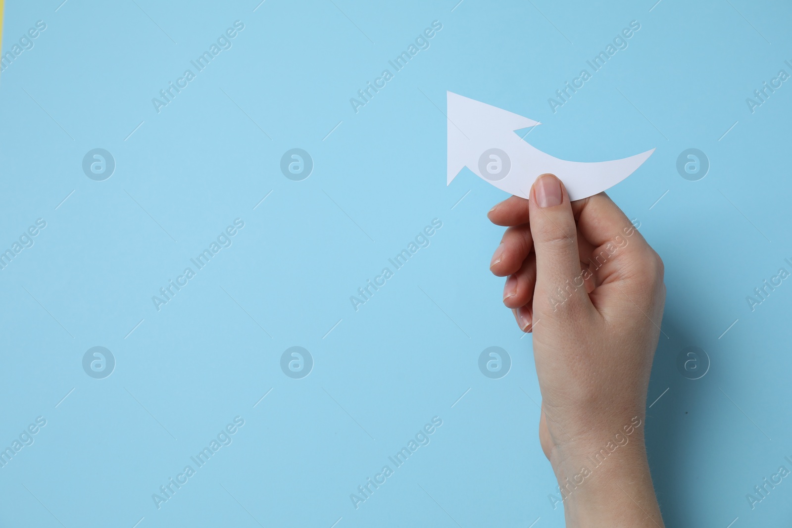 Photo of Woman holding curved paper arrow on light blue background, top view. Space for text