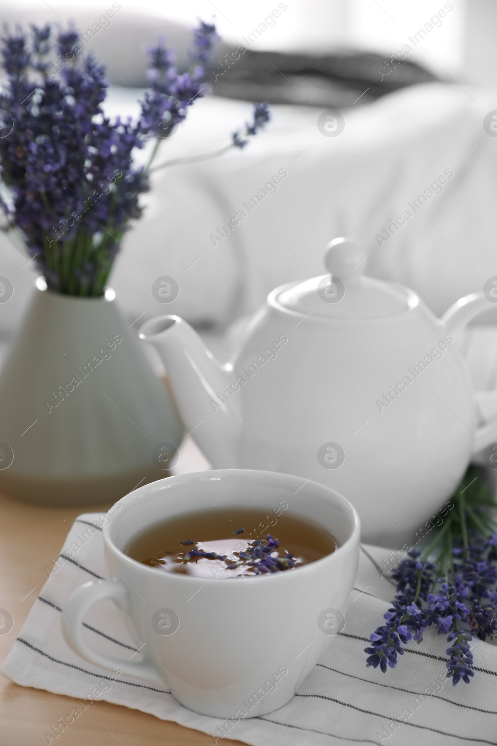 Photo of Wooden tray with cup of hot tea and beautiful lavender flowers on bed, closeup. Tasty breakfast