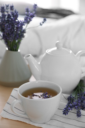 Wooden tray with cup of hot tea and beautiful lavender flowers on bed, closeup. Tasty breakfast