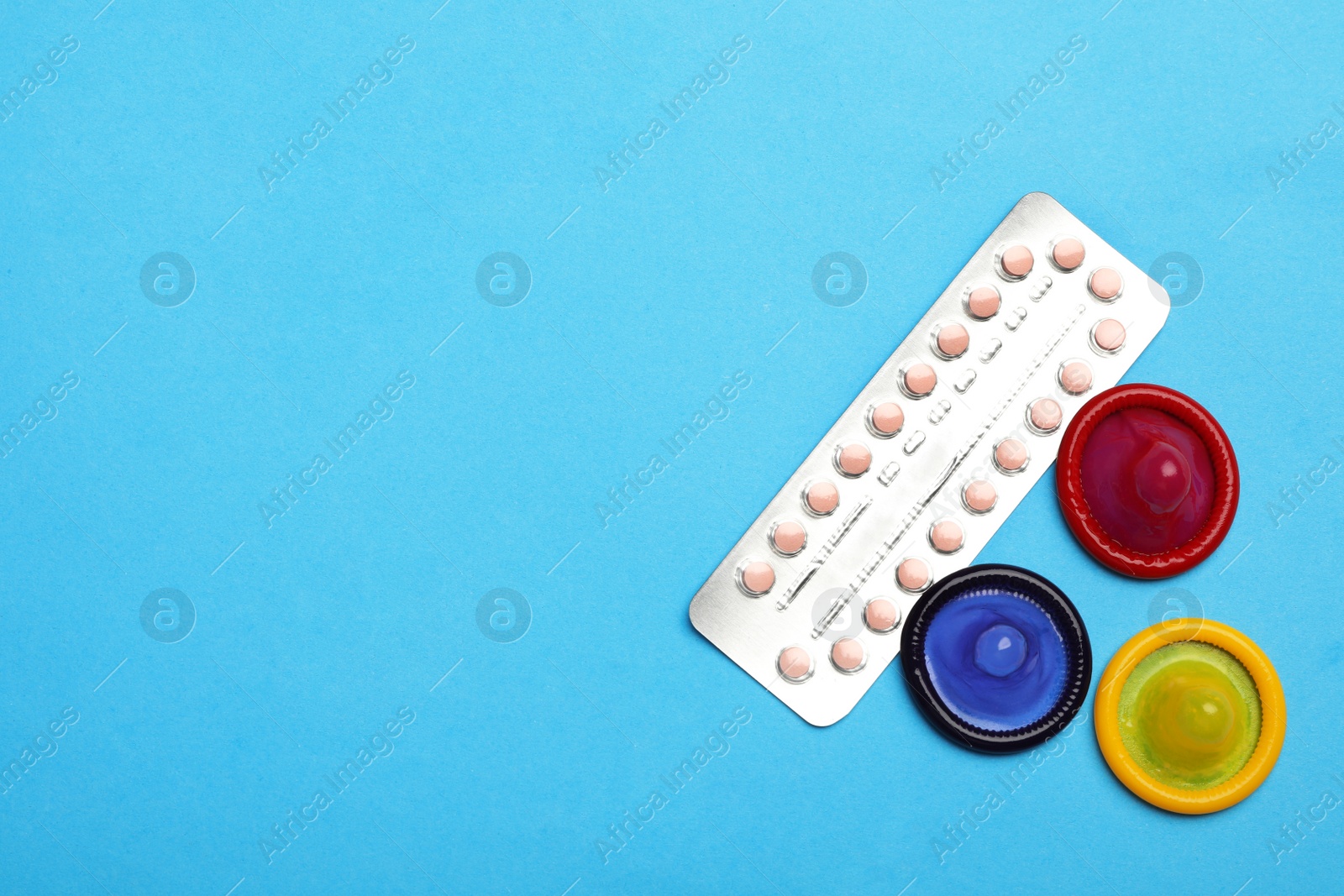 Photo of Condoms and birth control pills on light blue background, flat lay with space for text. Safe sex concept