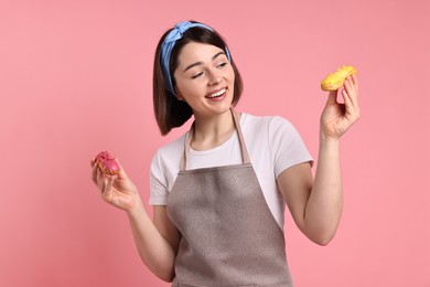 Happy confectioner with delicious eclairs on pink background