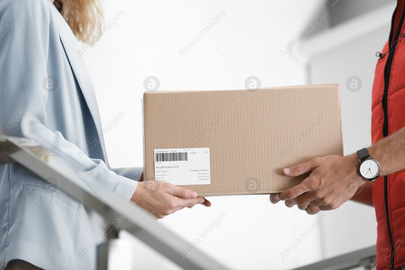 Photo of Young woman receiving parcel from courier indoors