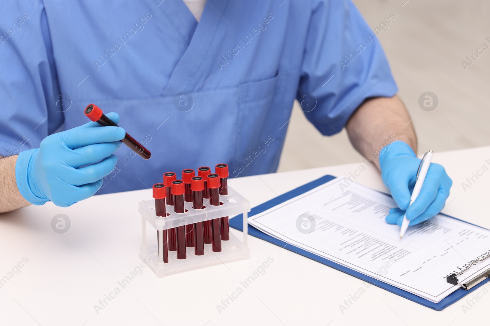 Photo of Doctor with samples of blood in test tubes at white table, closeup