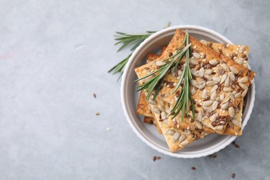 Photo of Cereal crackers with flax, sunflower, sesame seeds and rosemary in bowl on grey table, top view. Space for text