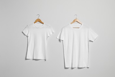 Photo of Hangers with different t-shirts on light wall. Mockup for design