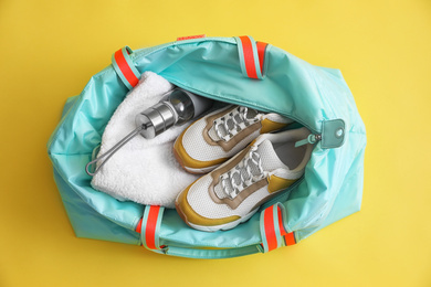 Gym bag with sports equipment on yellow background, top view