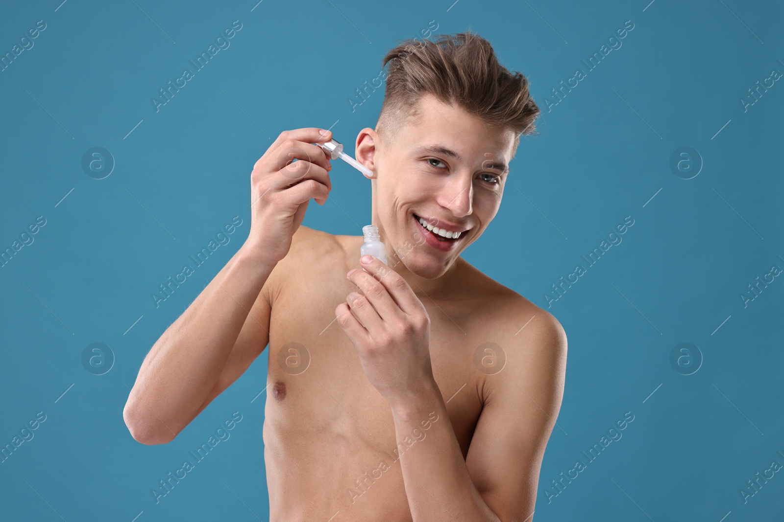 Photo of Handsome man applying serum onto his face on blue background