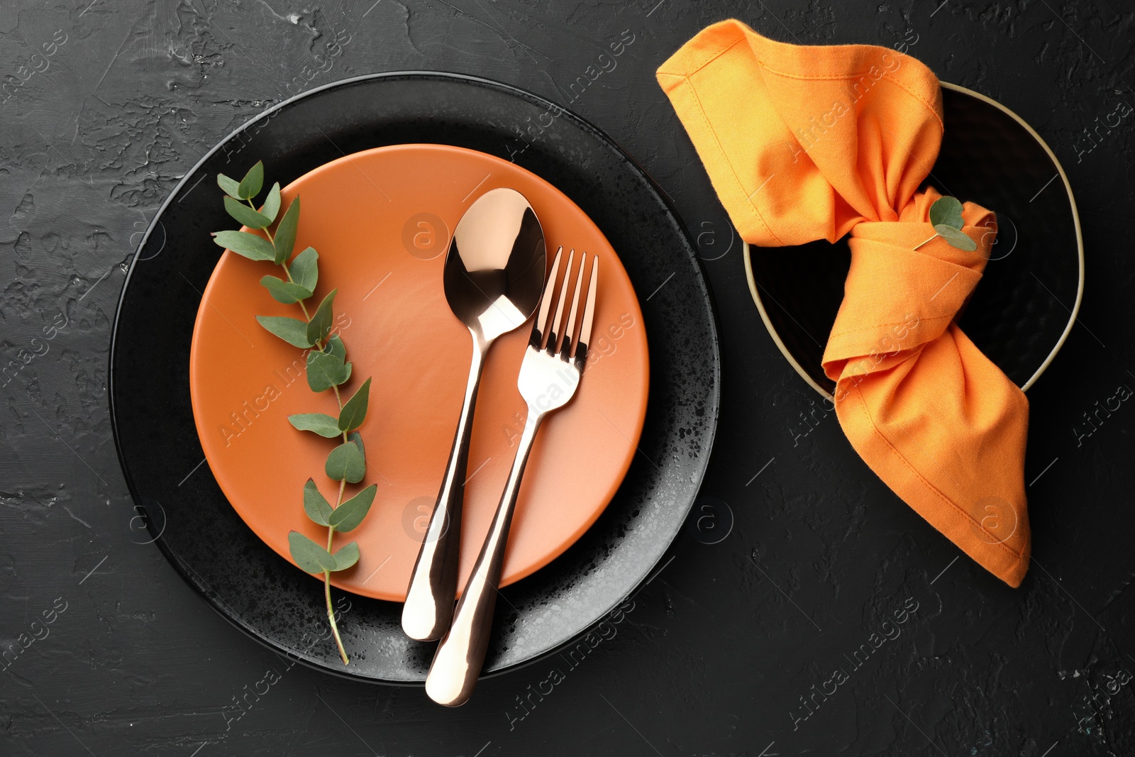 Photo of Stylish setting with cutlery, eucalyptus branch, napkin and plates on dark textured table, flat lay