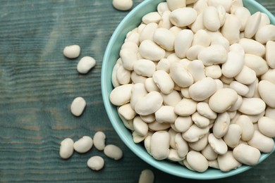 Photo of Bowl of uncooked white beans on blue wooden table, top view. Space for text