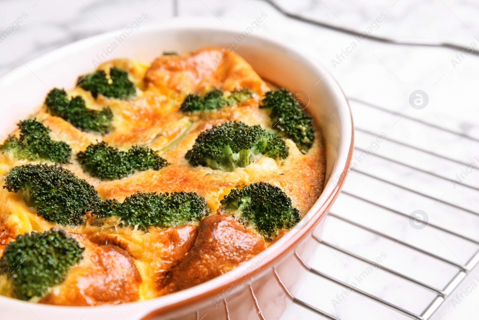 Photo of Tasty broccoli casserole in baking dish on cooling rack, closeup