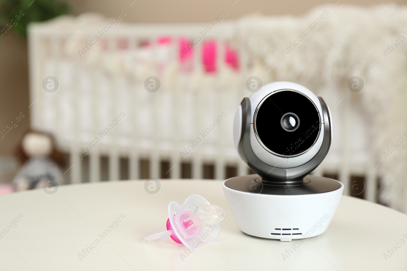 Photo of Modern CCTV security camera and pacifier on table in nursery. Space for text