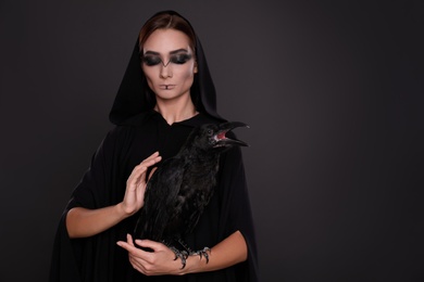 Mysterious witch with raven on black background, space for text