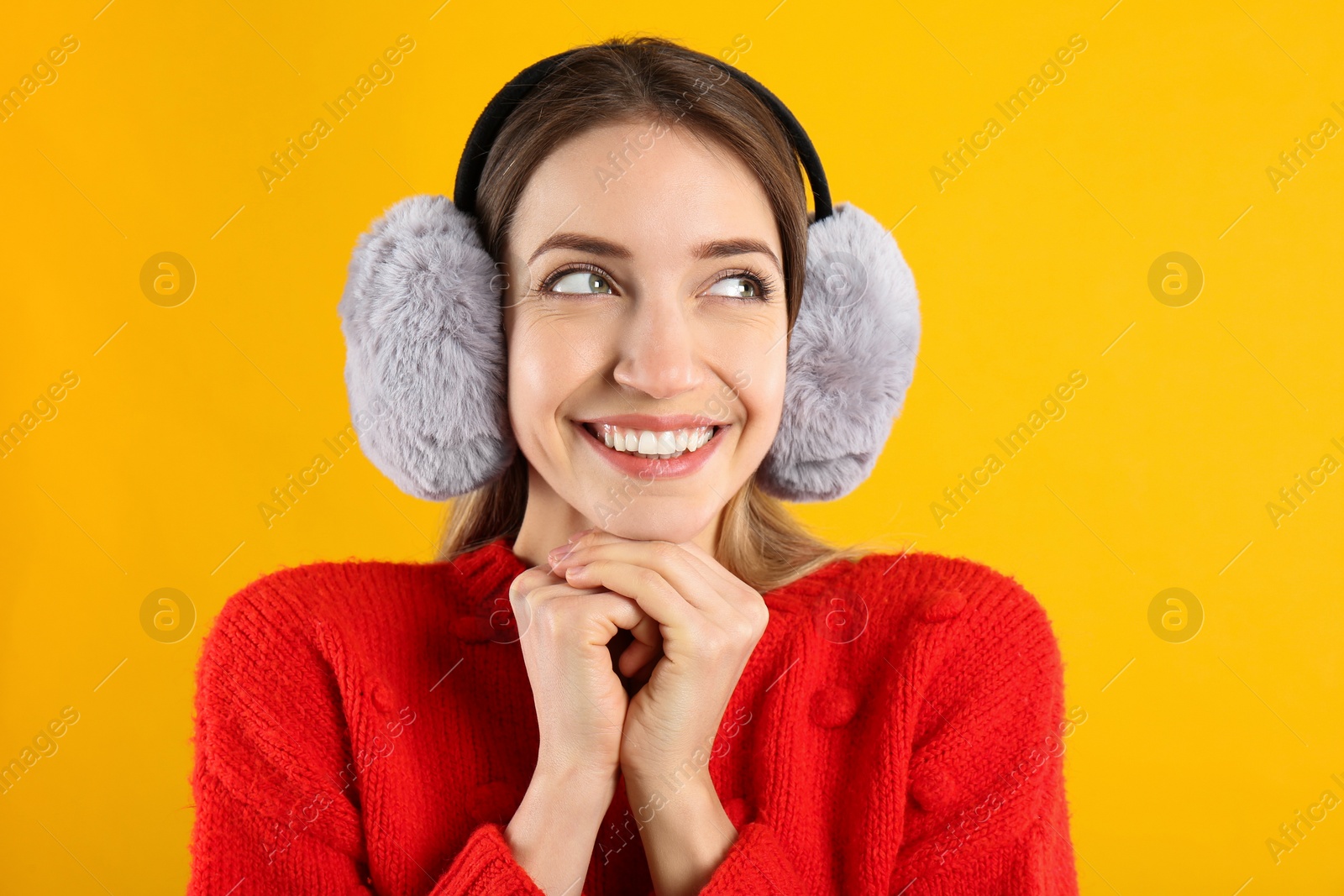 Photo of Happy woman wearing warm earmuffs on yellow background