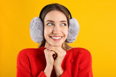 Happy woman wearing warm earmuffs on yellow background