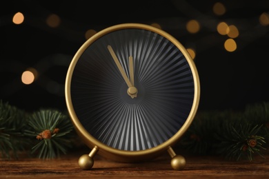 Photo of Stylish clock with decor on wooden table against blurred Christmas lights, closeup. New Year countdown