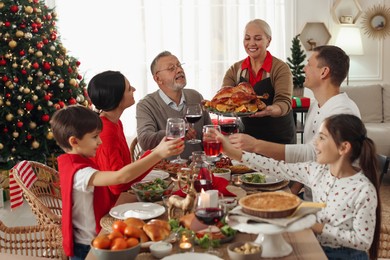 Happy family clinking glasses of drinks at festive dinner indoors. Christmas celebration