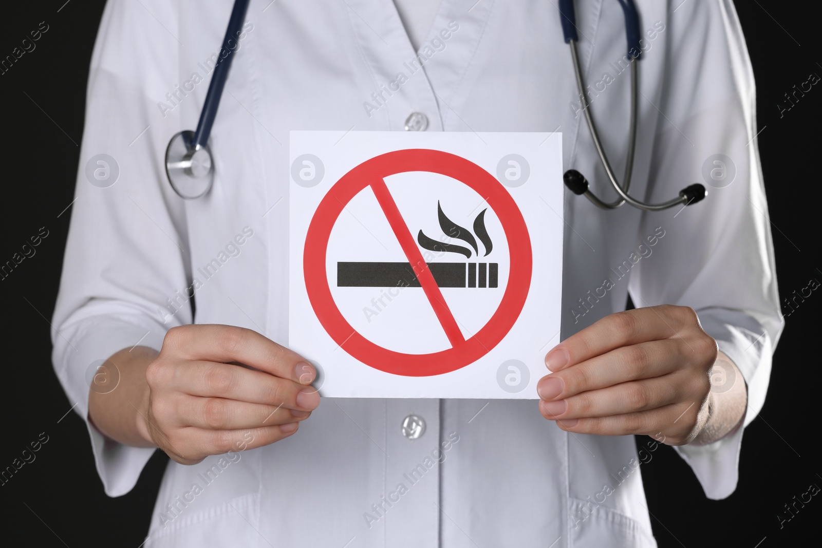 Photo of Doctor holding card with no smoking sign on black background, closeup