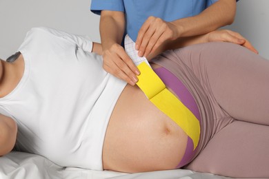 Photo of Pregnant woman visiting physiotherapist. Doctor applying kinesio tape on couch, closeup