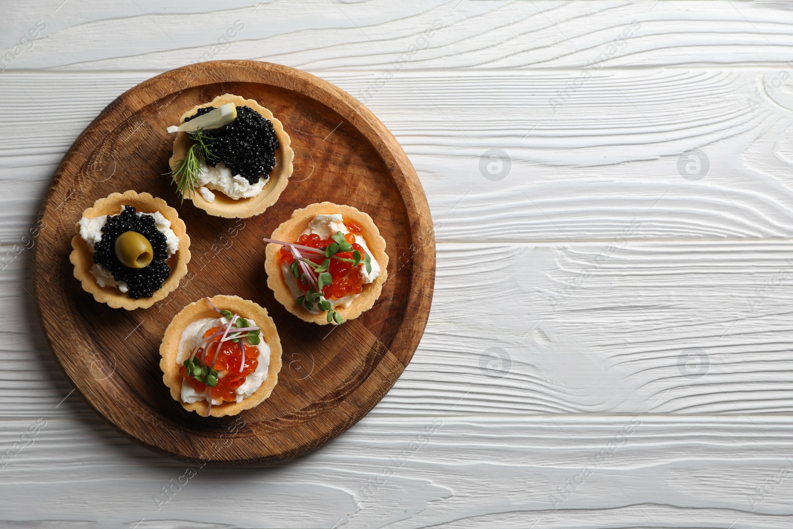 Photo of Delicious tartlets with red and black caviar served on white wooden table, top view. Space for text