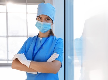 Doctor in medical gloves, protective mask and scrubs indoors. Space for text