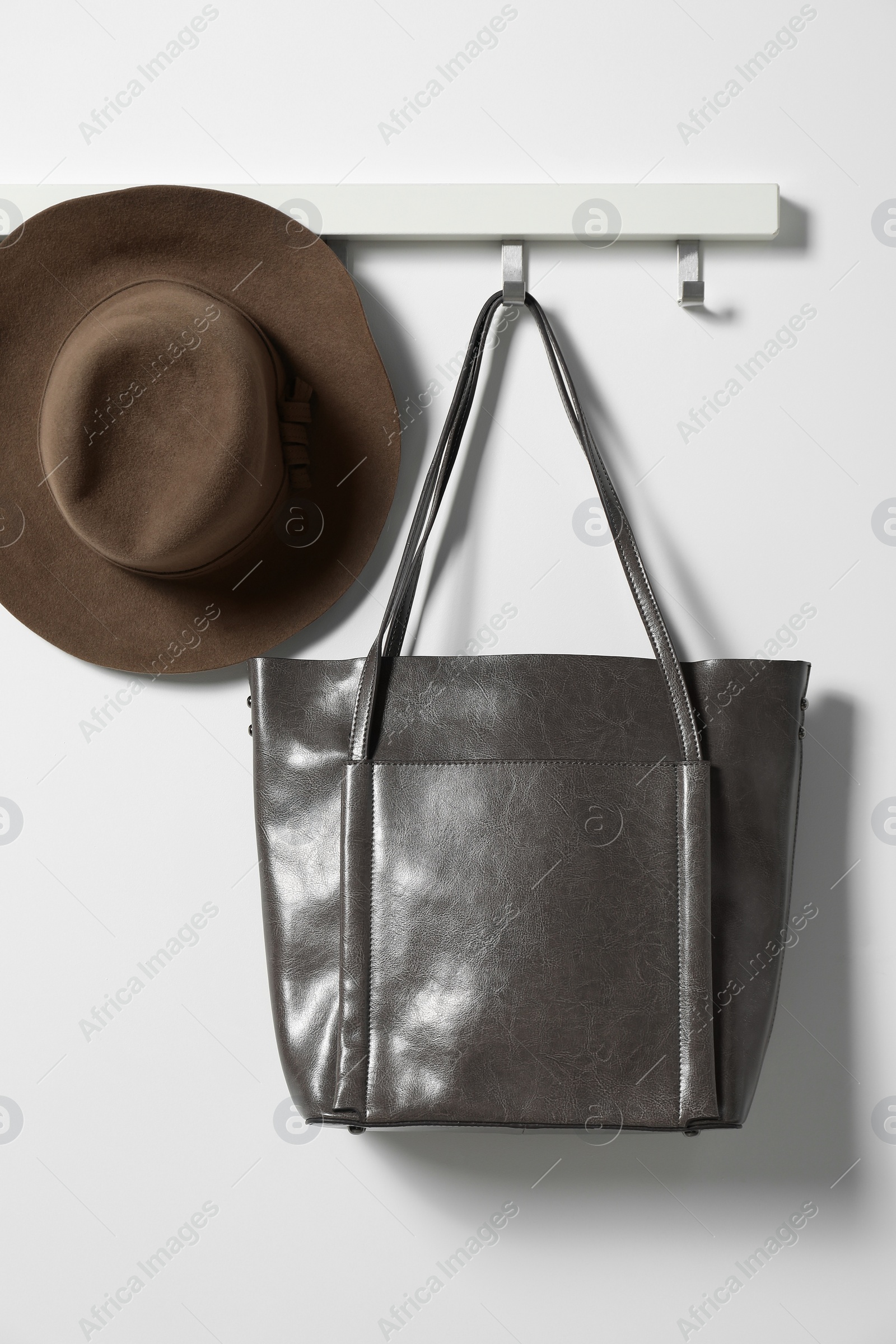 Photo of Brown hat and bag hanging on hook rack on white wall