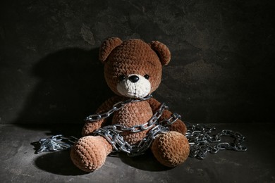 Stop child abuse. Chained toy bear in dark room