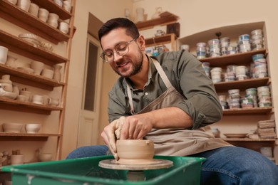 Photo of Clay crafting. Happy man making bowl on potter's wheel in workshop, low angle view