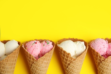Delicious ice creams in wafer cones on yellow background, flat lay. Space for text