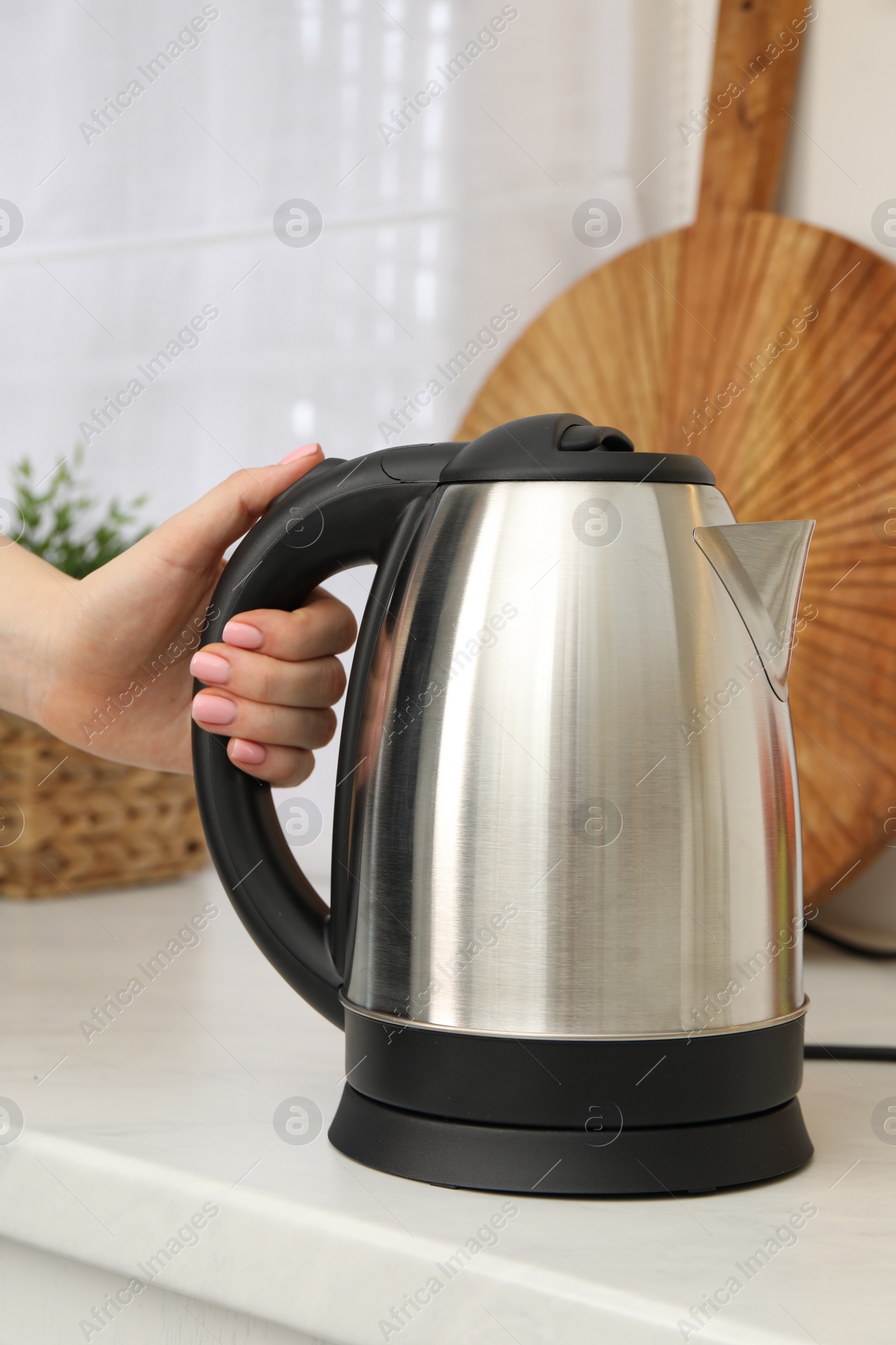 Photo of Woman with electric kettle in kitchen, closeup