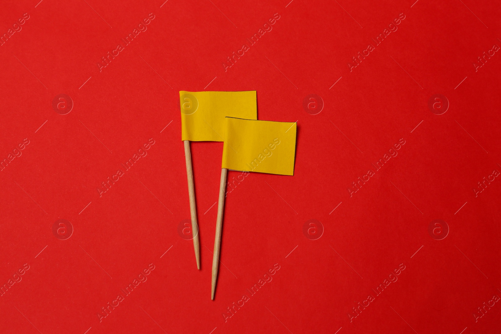 Photo of Small yellow paper flags on red background, flat lay