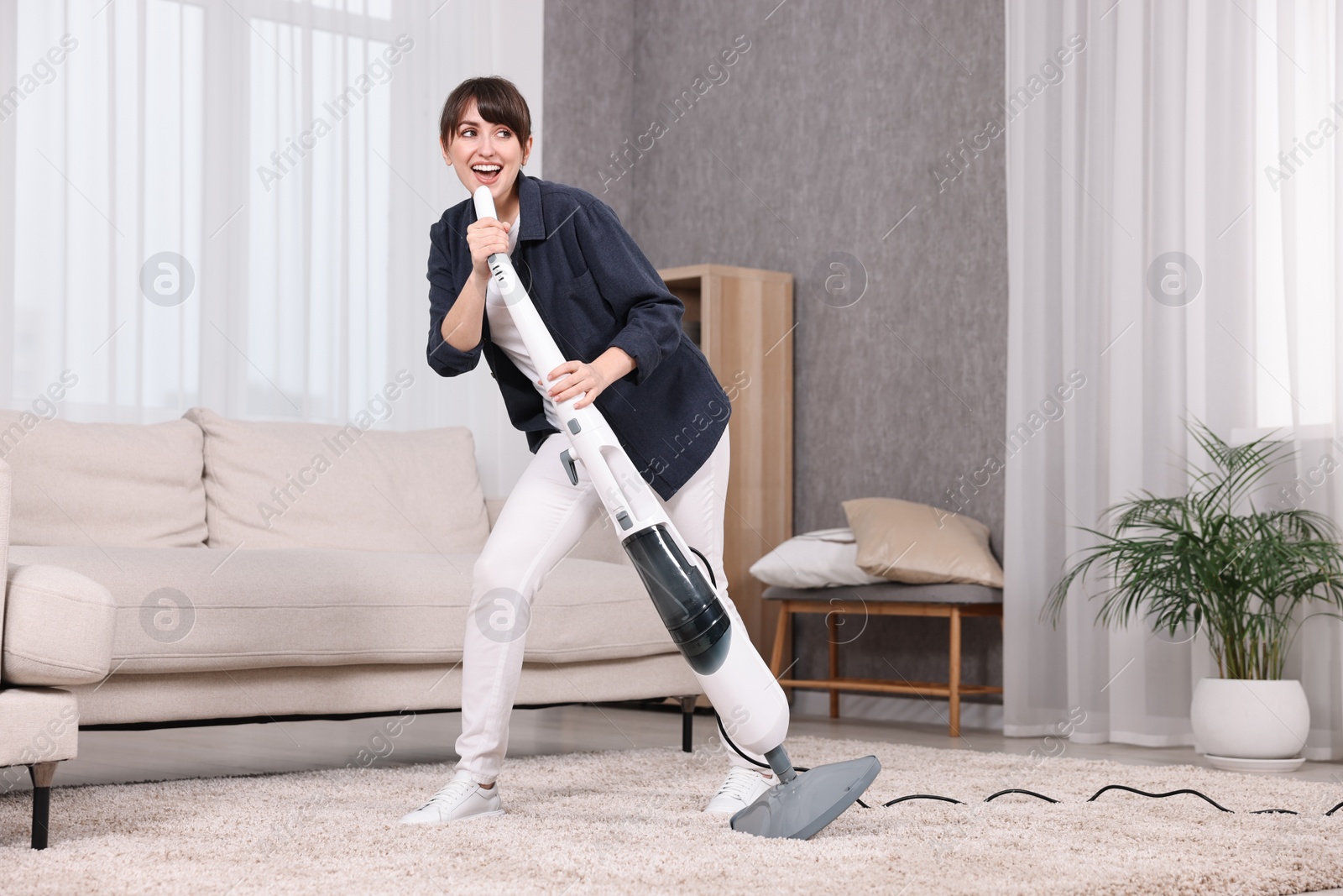 Photo of Happy young housewife having fun while cleaning carpet at home