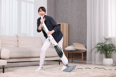 Happy young housewife having fun while cleaning carpet at home