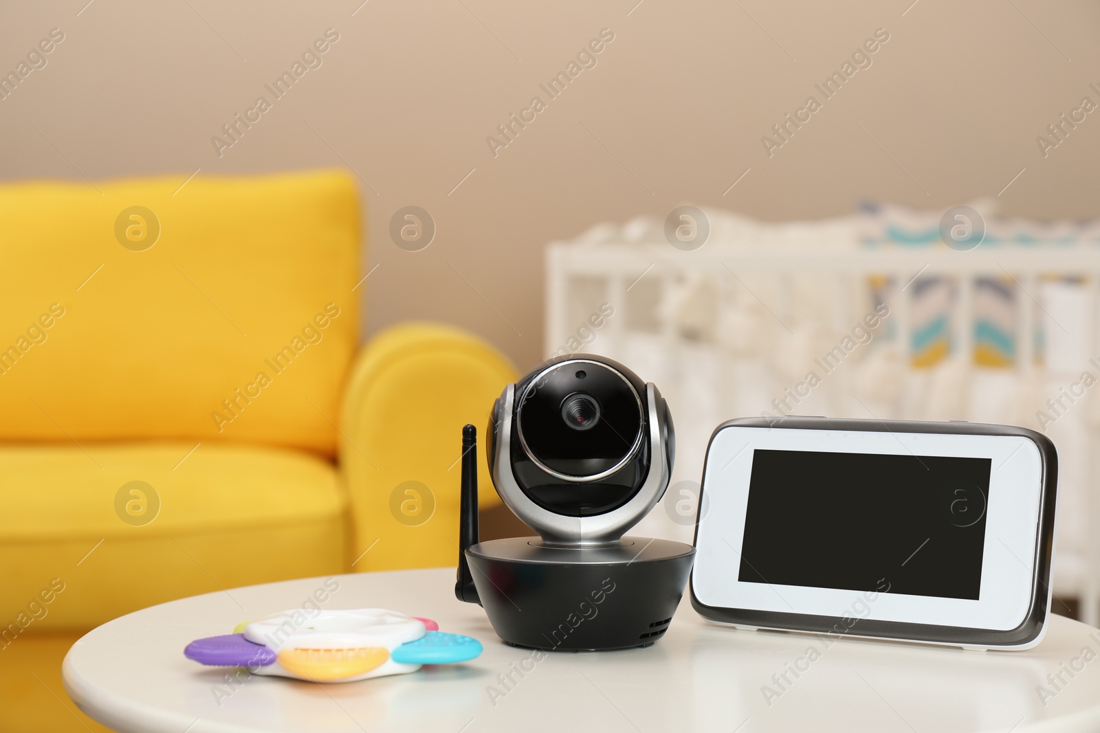 Photo of Modern CCTV security camera, monitor and teether on table in nursery. Space for text