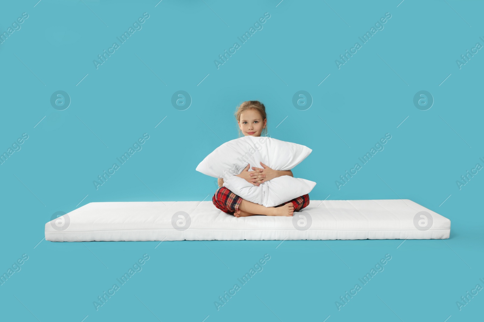Photo of Little girl hugging pillow on mattress against light blue background