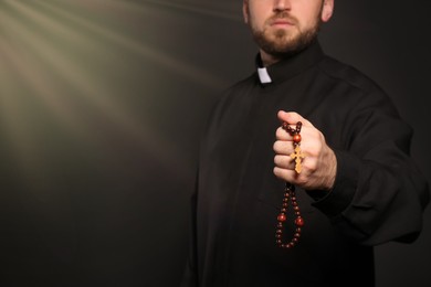 Image of Holy light and priest with rosary beads on black background, closeup. Space for text