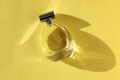 Photo of Luxury women's perfume. Sunlit glass bottle on yellow background, top view