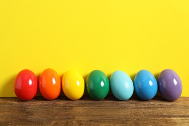 Easter eggs on wooden table against yellow background, space for text