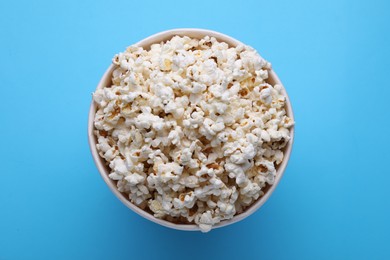 Photo of Paper bucket with delicious popcorn on light blue background, top view