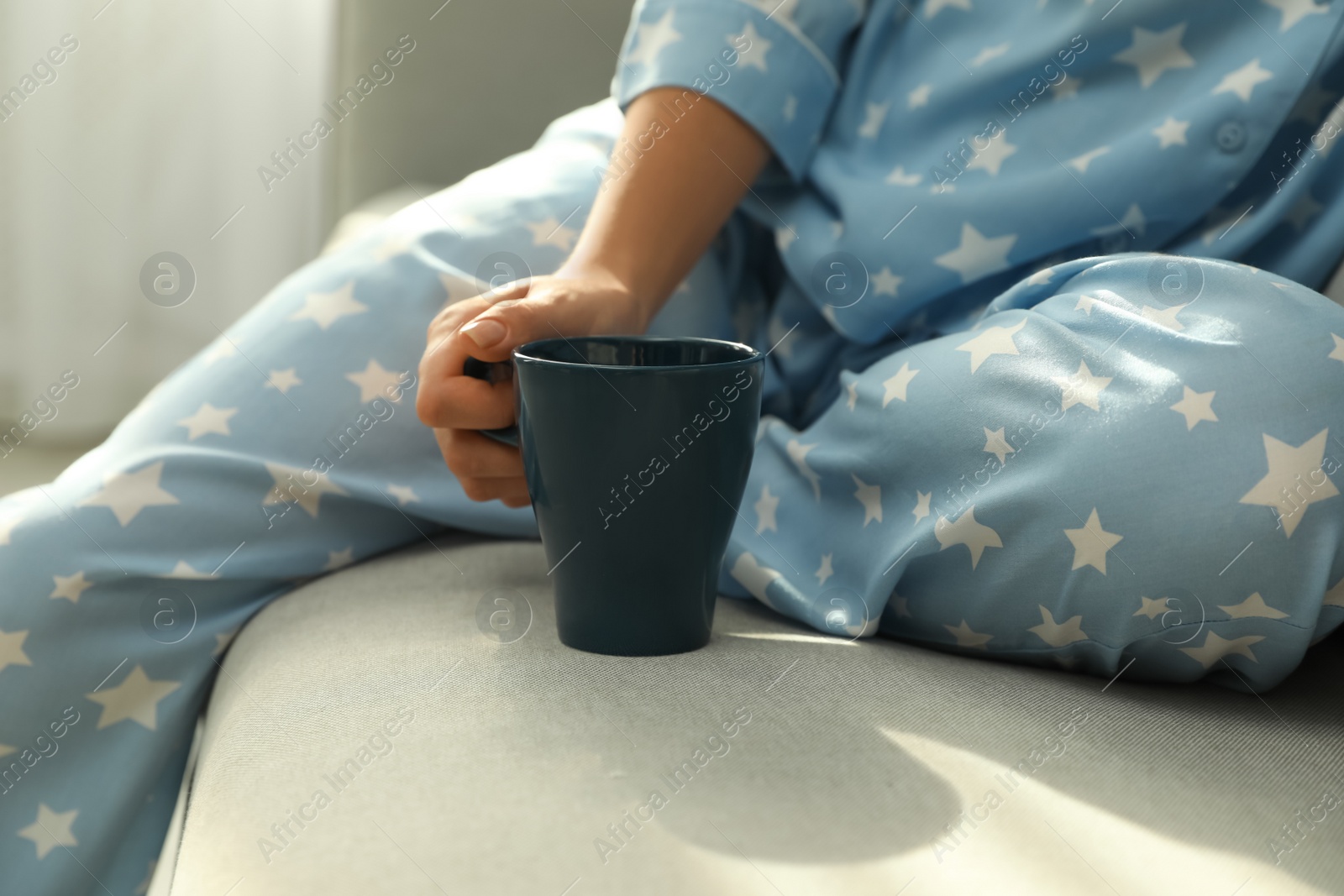 Photo of Woman in pajamas with cup sitting on sofa at home, closeup